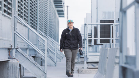 Female datacenter employee walks outside next to cooling towers